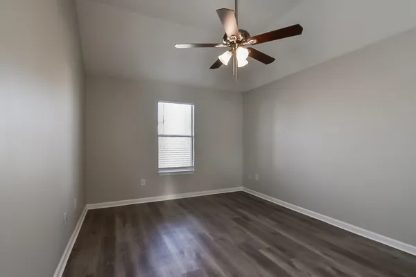 an empty room with wooden floor fan and windows