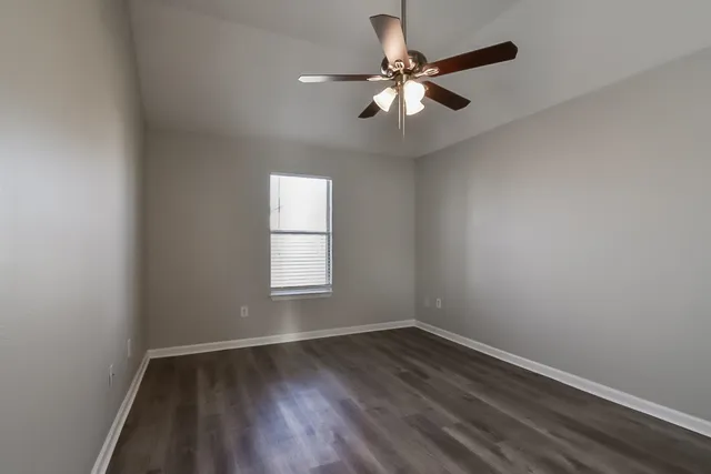 an empty room with wooden floor fan and windows