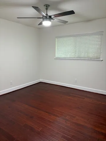 a view of an empty room with wooden floor and a ceiling fan