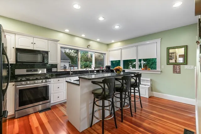 a kitchen with stainless steel appliances granite countertop a stove top oven a sink dishwasher a dining table and chairs with wooden floor