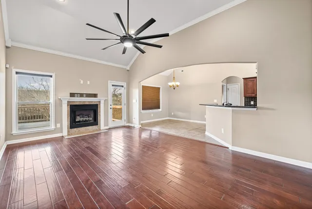 an empty room with wooden floor a ceiling fan a fireplace and windows