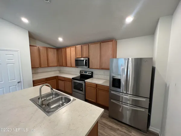 a kitchen with granite countertop wooden cabinets a refrigerator and a stove top oven with wooden floor