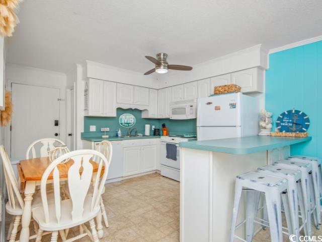 9530 Shore Drive, Unit 2D Myrtle Beach, SC 29572 - Photo 4 of 25 Kitchen with a kitchen breakfast bar, white appliances, a ceiling fan, and white cabinetry