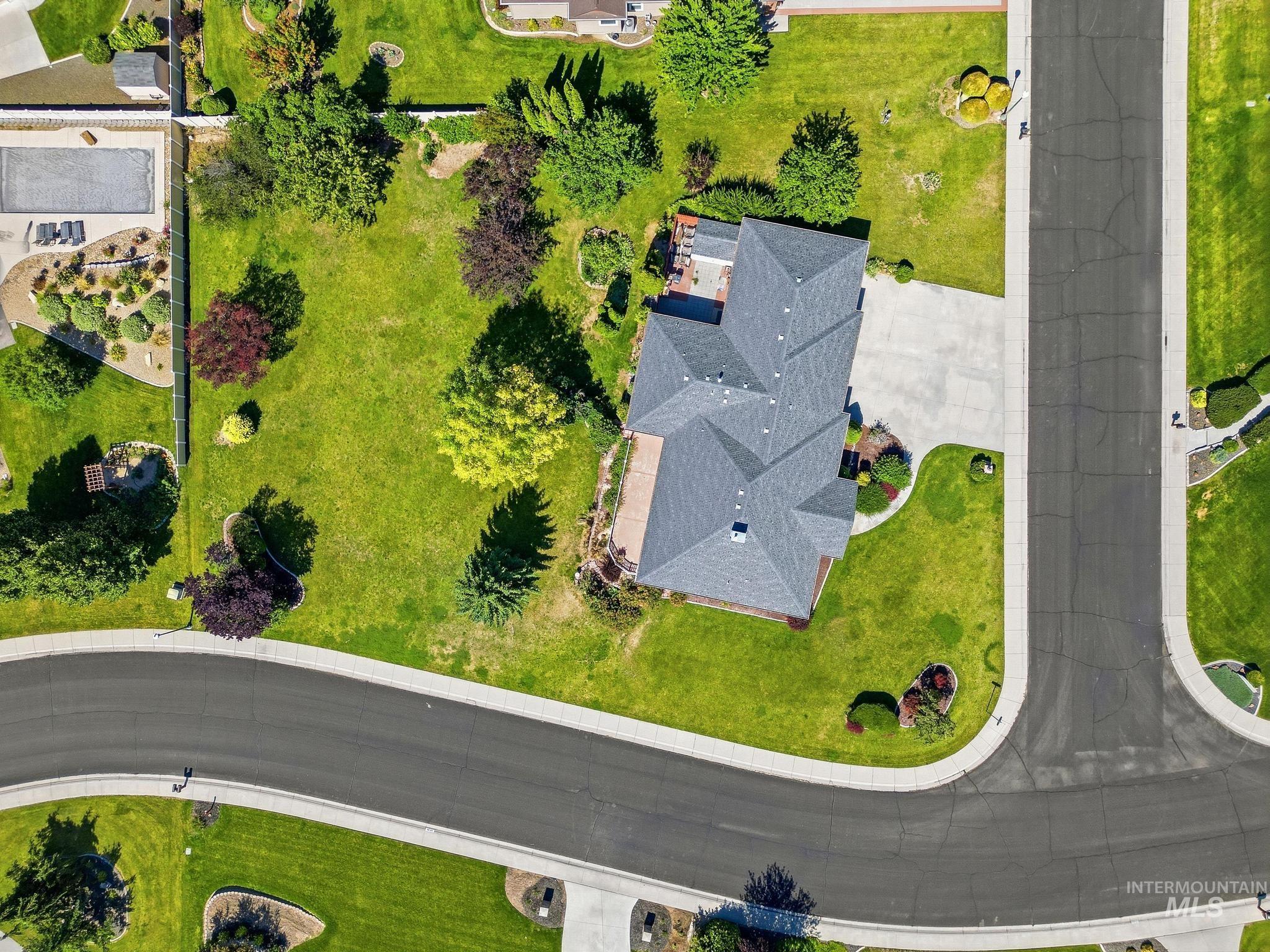 15181 Drury Way Caldwell, ID 83607 - Photo 46 of 49 Expansive property featuring a grey shingle roof, lush green lawn, mature trees, a paved driveway, and a backyard patio