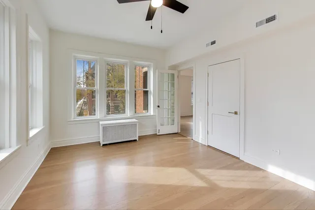 an empty room with chandelier fan and windows