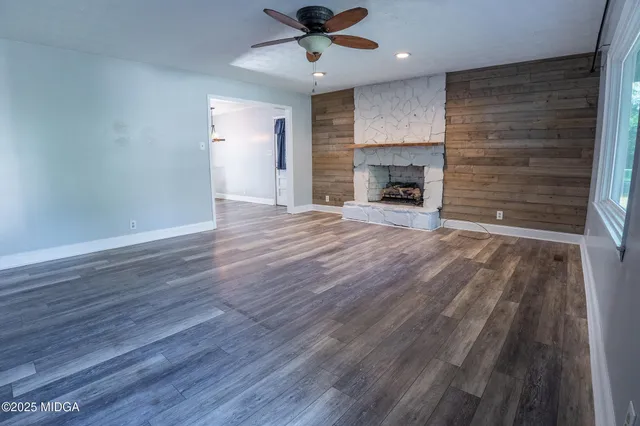 an empty room with wooden floor a ceiling fan a fireplace and windows