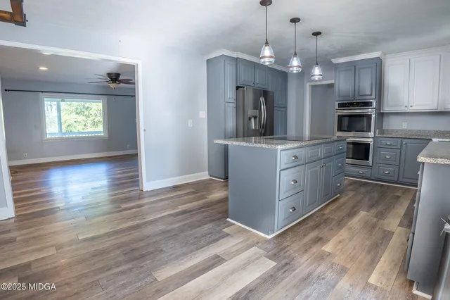 a kitchen with stainless steel appliances granite countertop a refrigerator a sink dishwasher a oven and a dining table with wooden floor