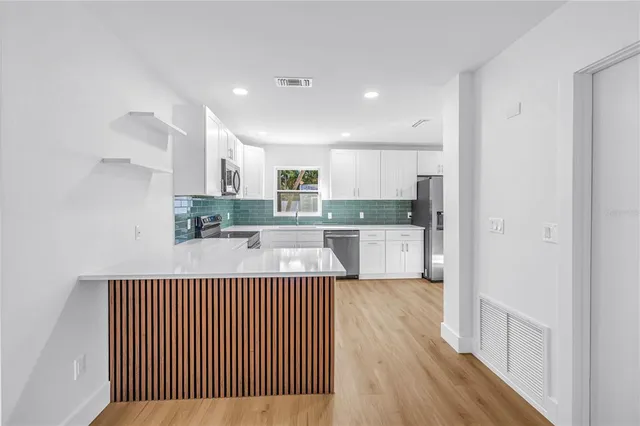 a open kitchen with kitchen island a stove a refrigerator cabinets and a wooden floor