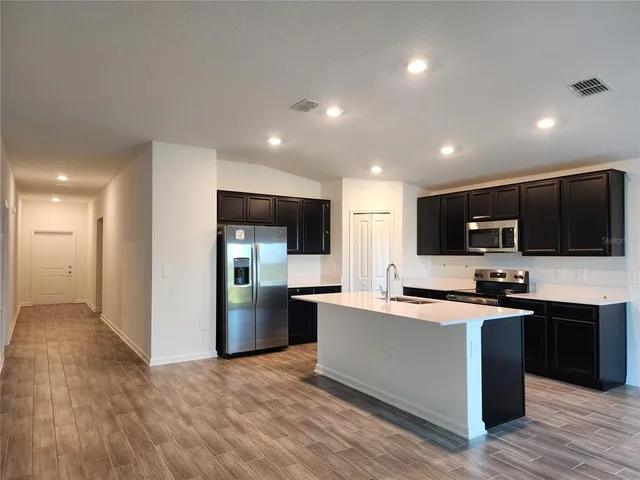 a kitchen with stainless steel appliances kitchen island a sink dishwasher a refrigerator and a stove with wooden floor