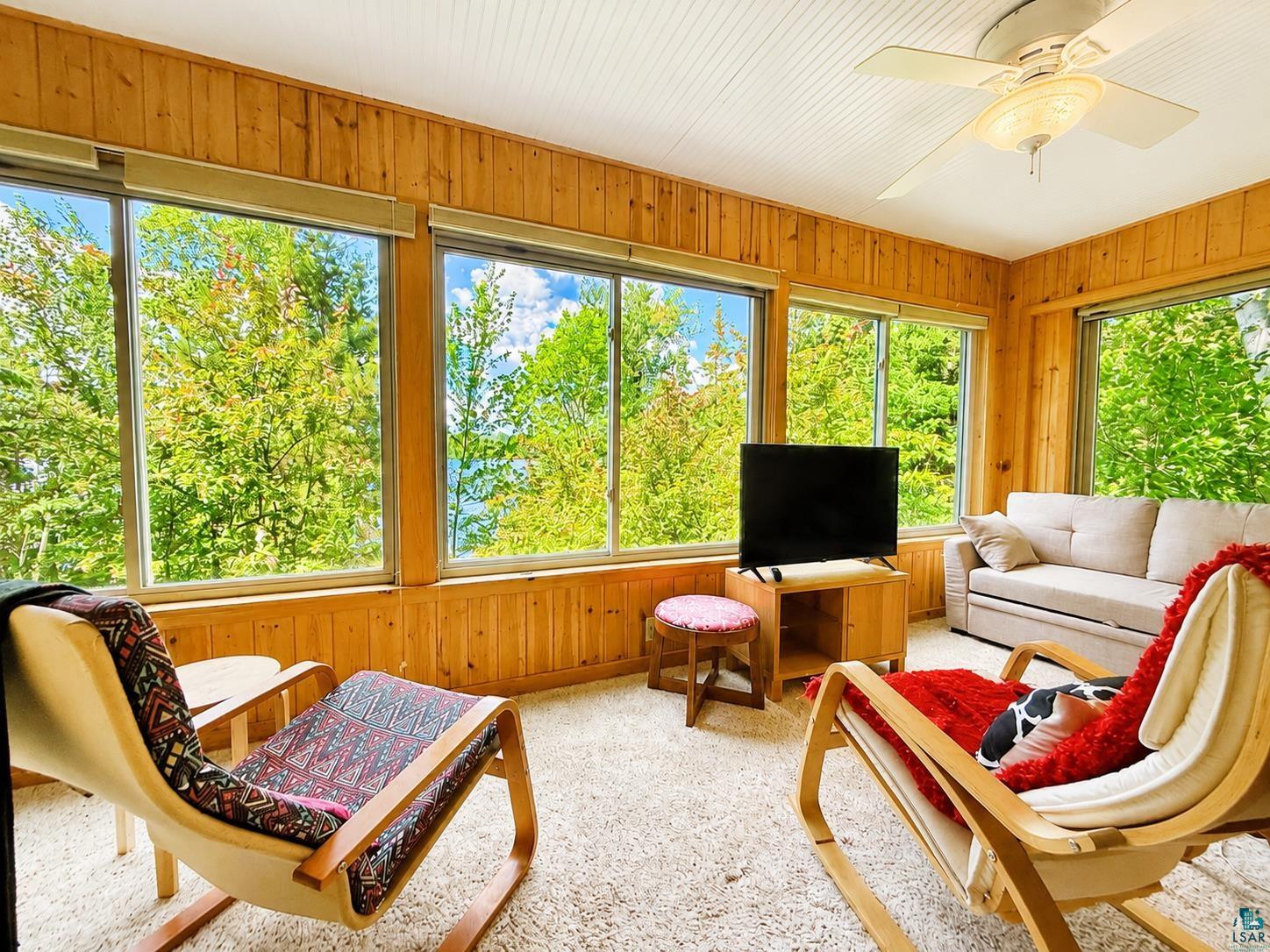 1787 North Bay Road Ely, MN 55731 - Photo 14 of 40 Sunroom featuring expansive perimeter windows, natural wood paneling, a white beadboard ceiling, and plush neutral carpeting