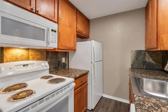 a kitchen with stainless steel appliances granite countertop a refrigerator a stove and a sink with wooden floor