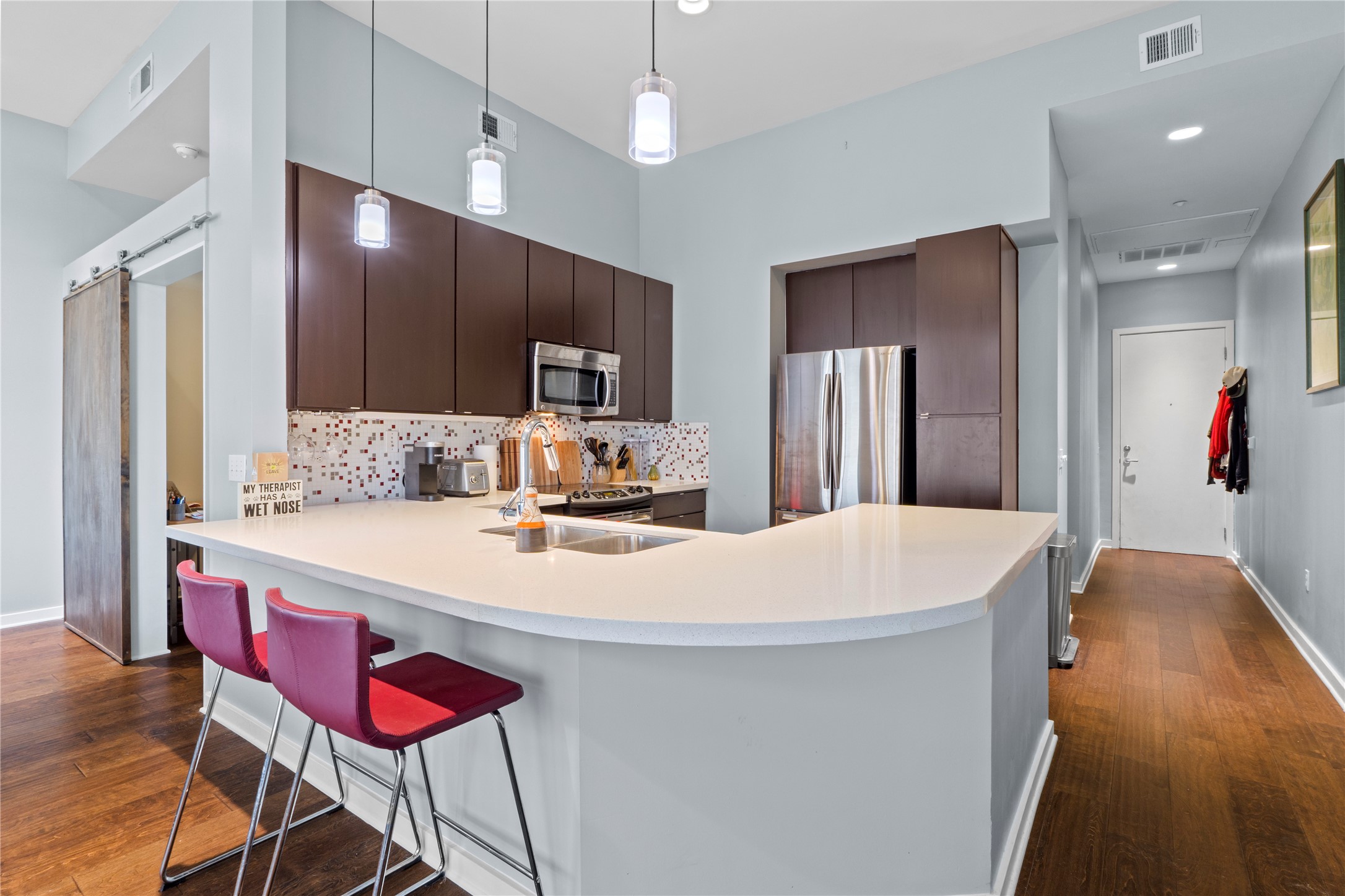 507 Sabine Street, Unit 509 Austin, TX 78701 - Photo 4 of 23 Kitchen with dark brown cabinets, decorative backsplash, pendant lighting, dark wood-style flooring, and stainless steel appliances