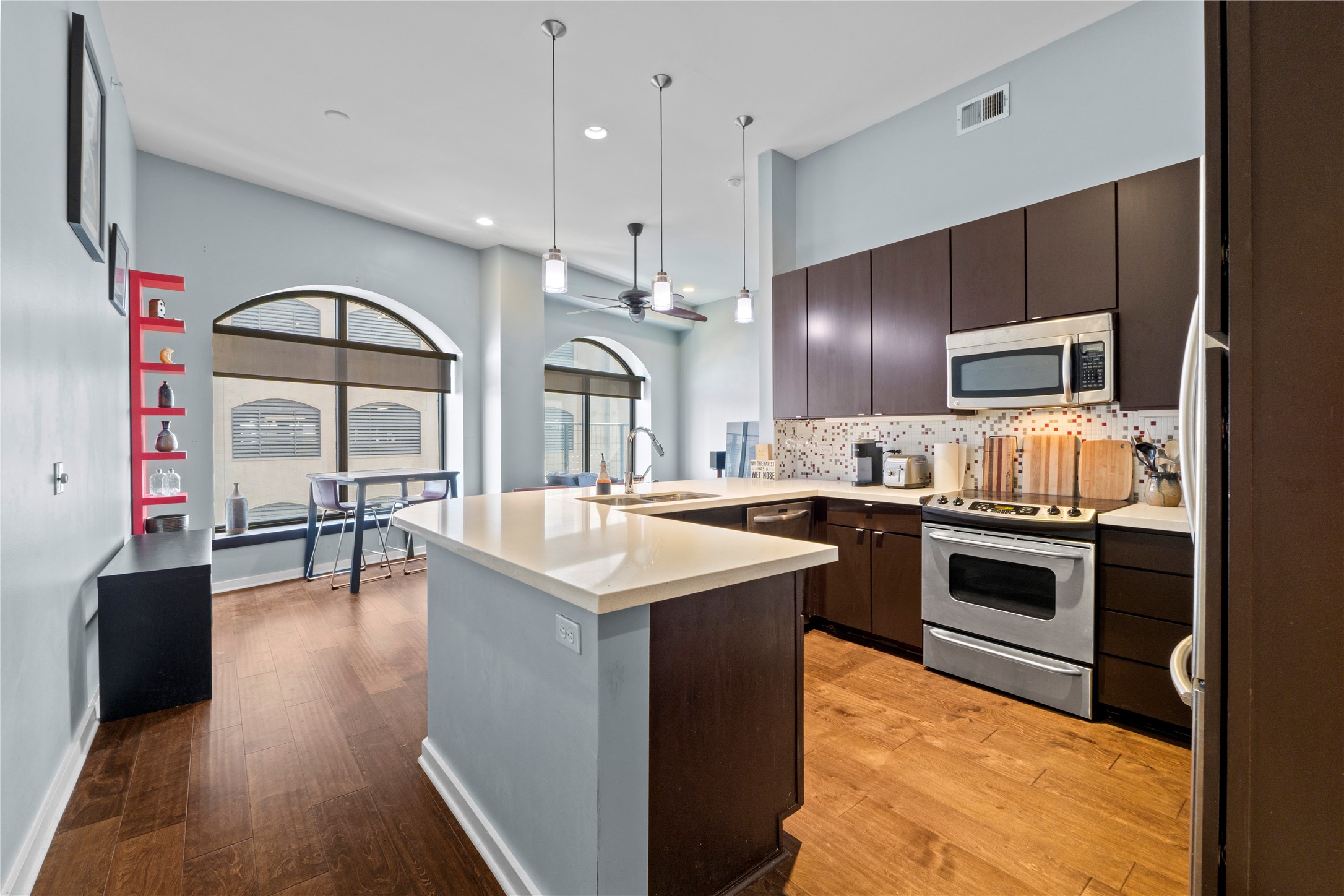 507 Sabine Street, Unit 509 Austin, TX 78701 - Photo 7 of 23 Kitchen with dark brown cabinetry, appliances with stainless steel finishes, a peninsula, decorative backsplash, and light wood finished floors
