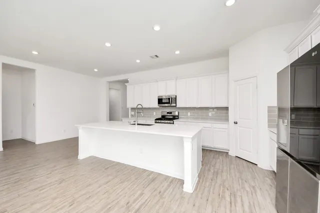 a large white kitchen with wooden floor and stainless steel appliances