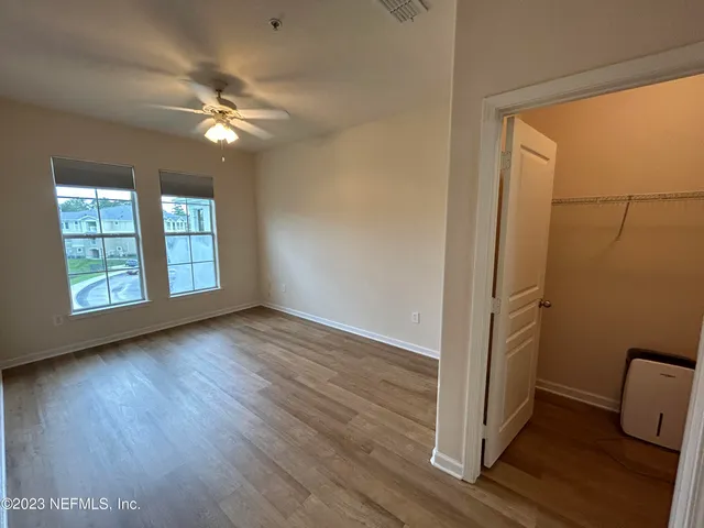 an empty room with wooden floor fan and windows