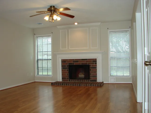 a view of an empty room with wooden floor fireplace and a window