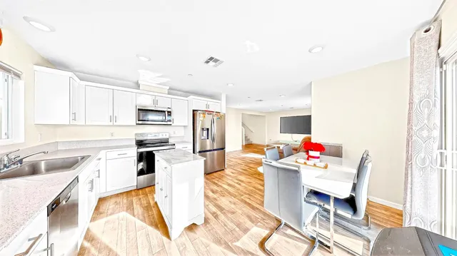 a open kitchen with stainless steel appliances kitchen island granite countertop a sink dishwasher and white cabinets with wooden floor