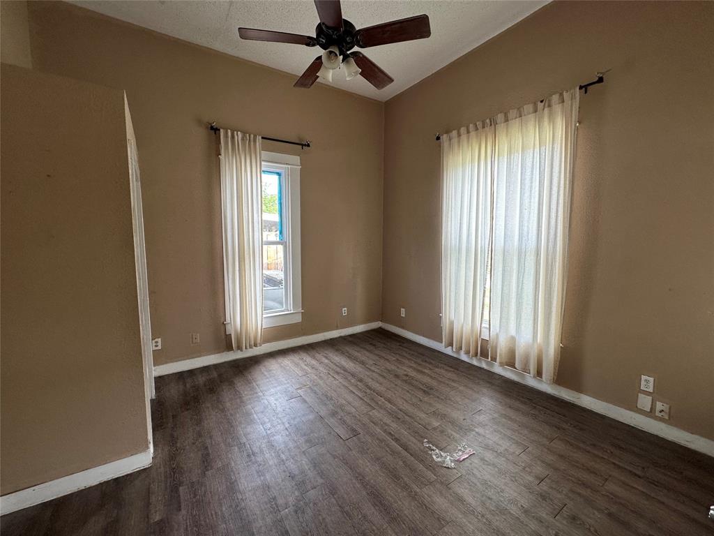 1405 Caddo Street Commerce, TX 75428 - Photo 5 of 8 an empty room with wooden floor fan and windows