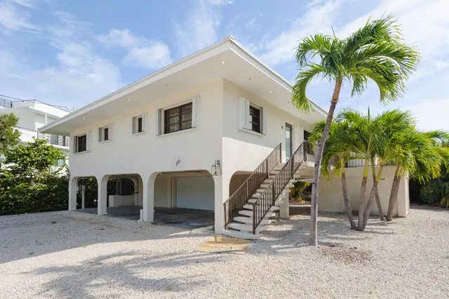 a view of a white house with a yard and palm trees
