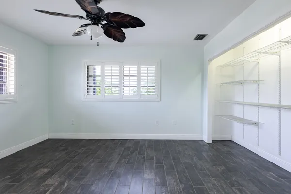 an empty room with wooden floor ceiling fan and windows