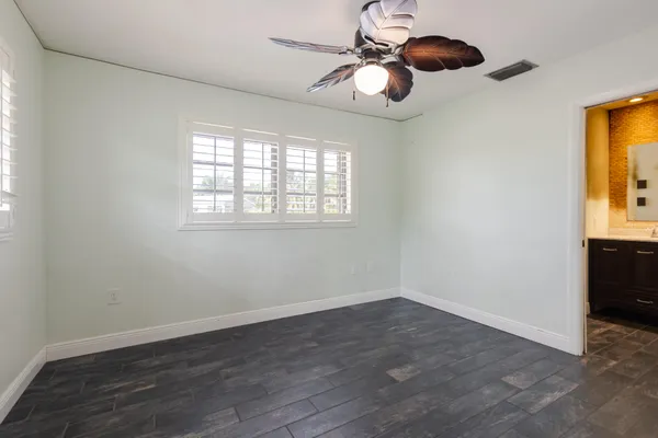 an empty room with wooden floor fan and windows