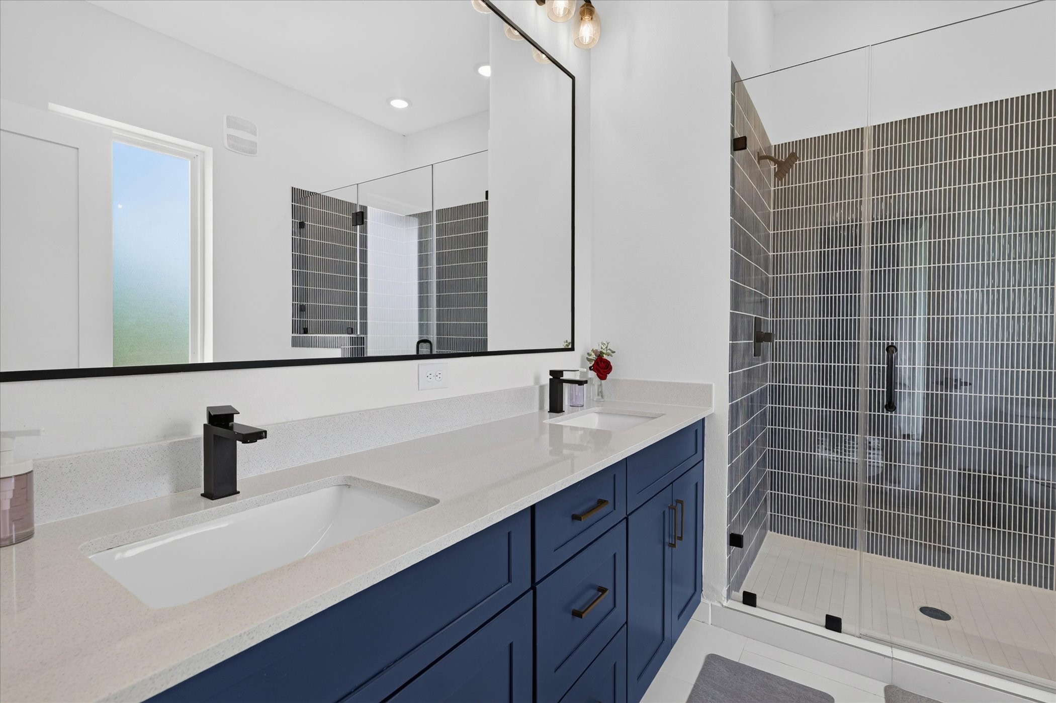 2000 Riverside Farms Road, Unit 8101 Austin, TX 78741 - Photo 23 of 41 This modern bathroom features a sleek double vanity with blue cabinets, black fixtures, and a large mirror. It includes a spacious glass-enclosed shower with stylish vertical tiles, creating a clean and contemporary look.