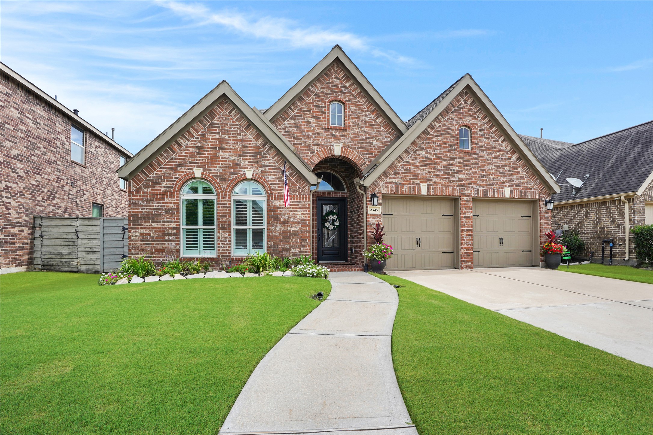 2345 Redwood Ridge Trail Manvel, TX 77578 - Photo 2 of 39 Charming brick home with a well-maintained front yard, featuring a two-car garage and a welcoming walkway leading to an arched entryway. The house has attractive window shutters and a neatly landscaped garden.