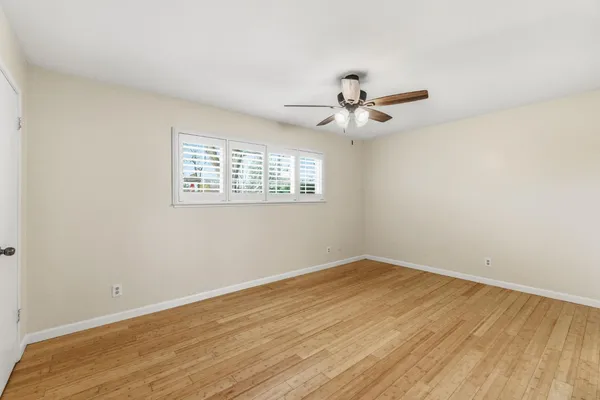 an empty room with wooden floor ceiling fan and windows
