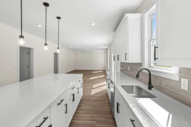 a view of empty room with wooden floor and kitchen view