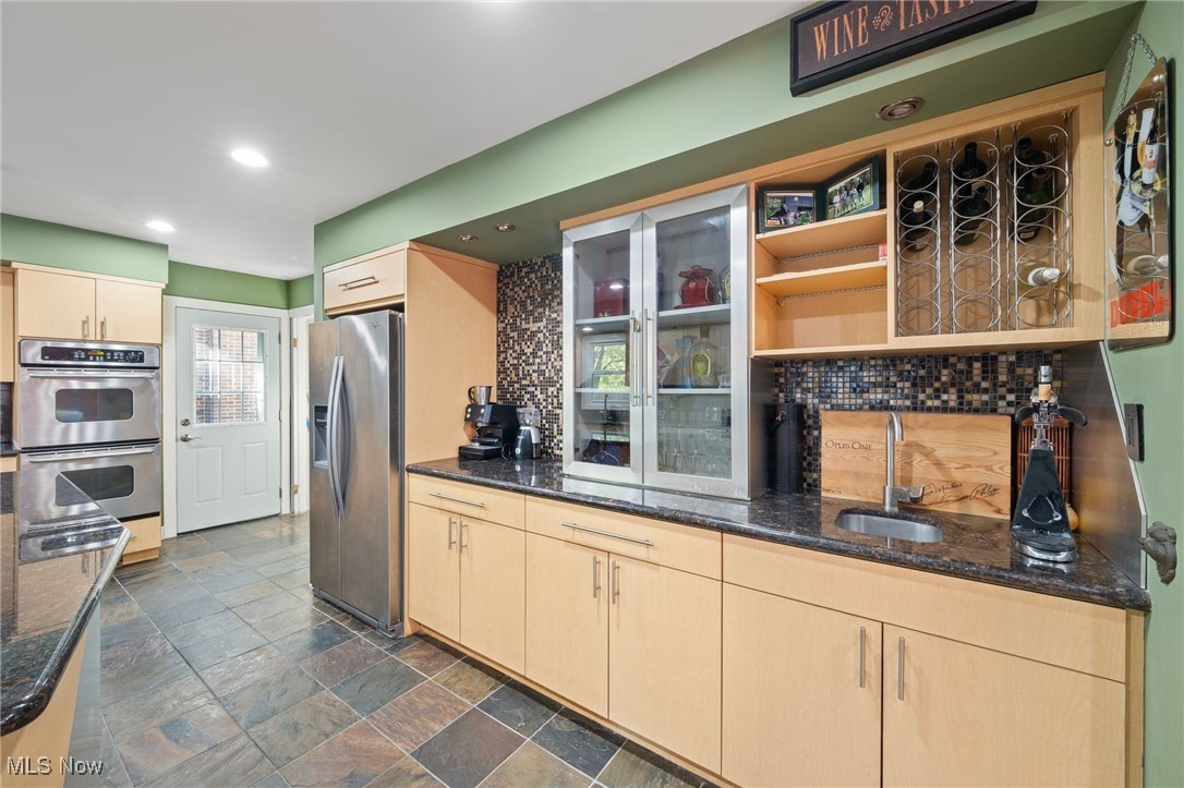 Kitchen with light brown cabinetry, appliances with stainless steel finishes, sink, and decorative backsplash