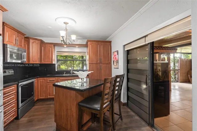 a kitchen with granite countertop stainless steel appliances a table chairs sink and refrigerator