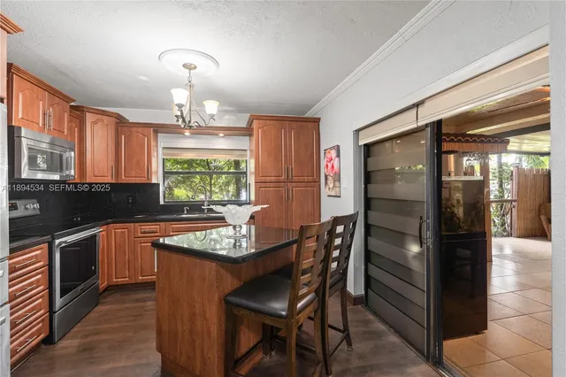 a kitchen with granite countertop stainless steel appliances a table chairs sink and refrigerator