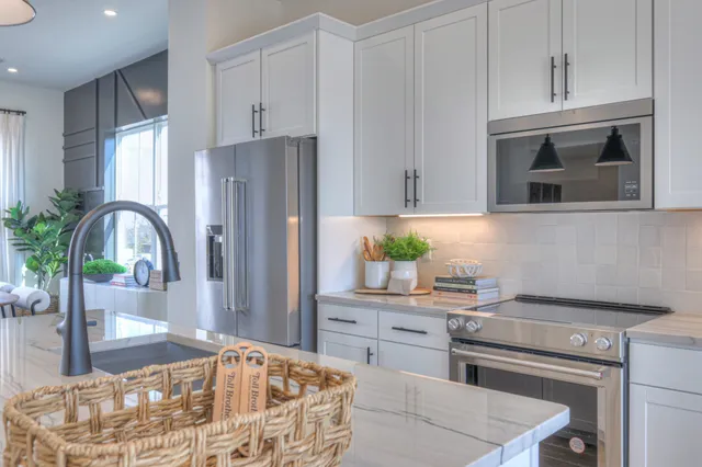 a kitchen with stainless steel appliances kitchen island granite countertop a refrigerator a stove a sink and white cabinets with wooden floor