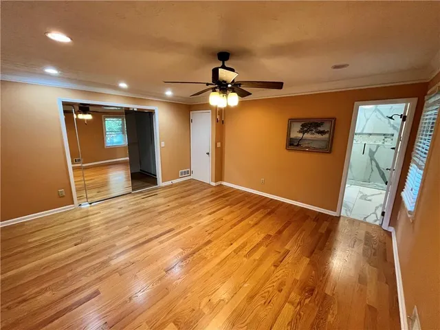 a view of an empty room with wooden floor and a ceiling fan