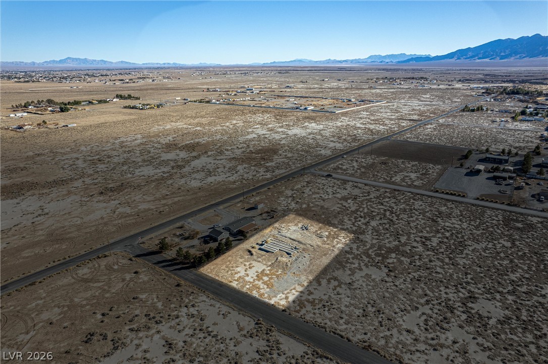 4051 Forest Road Pahrump, NV 89048 - Photo 8 of 15 A vast, level expanse of land awaits development, bordered by distant mountains under a clear sky.