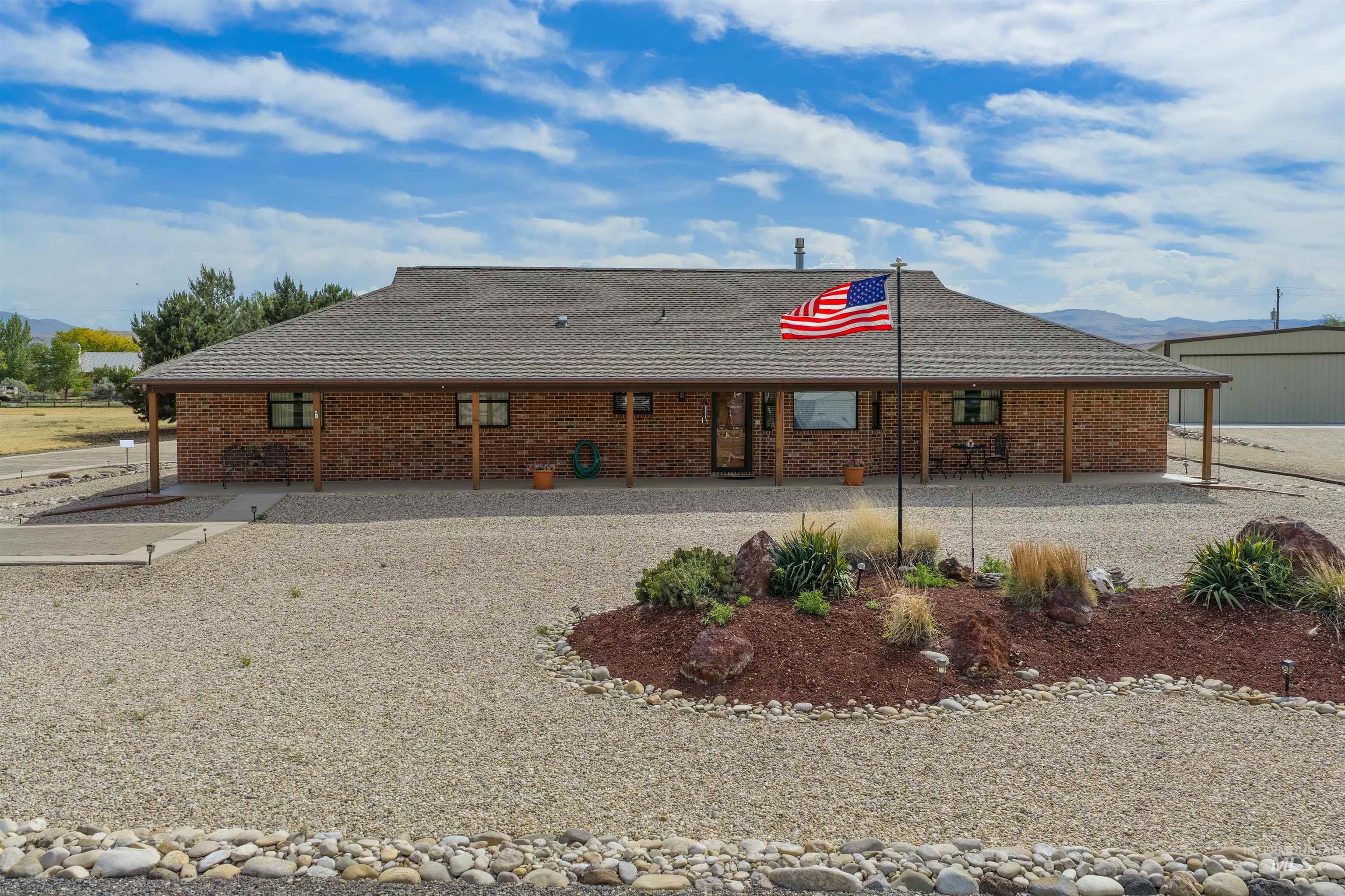 10514 Airpark Loop Road Melba, ID 83641 - Photo 8 of 47 Brick exterior residence featuring a covered front porch, gravel landscaping, and an ornamental planting bed