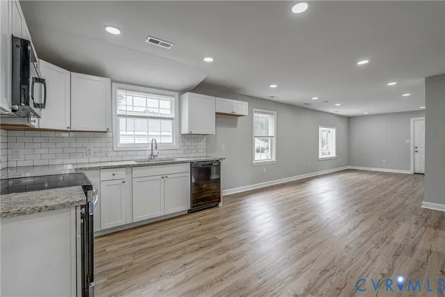 a kitchen with granite countertop wooden floors stainless steel appliances a sink and cabinets