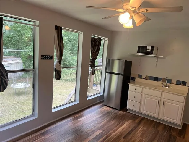 a kitchen with stainless steel appliances granite countertop a refrigerator a microwave a sink and white cabinets with wooden floor