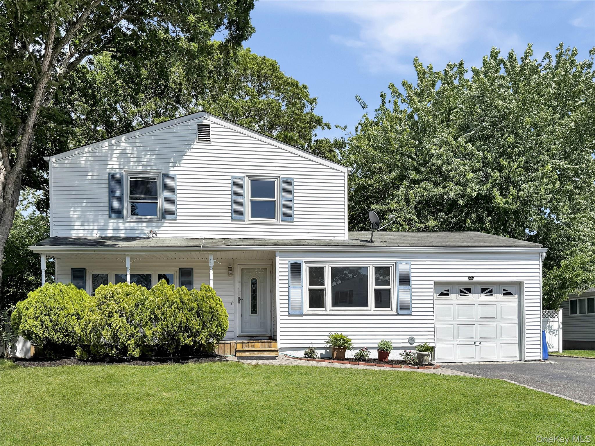 17 Belair Road Selden, NY 11784 - Photo 1 of 18 White siding exterior with blue window shutters, featuring a covered front porch, an attached garage, a paved driveway