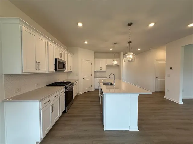 a large kitchen with stainless steel appliances granite countertop a large center island a stove a sink dishwasher and a refrigerator with wooden floor