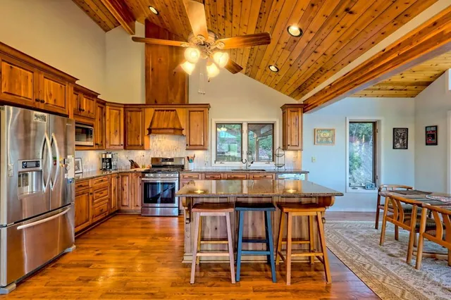 a kitchen with stainless steel appliances granite countertop a stove a refrigerator a kitchen island a dining table and chairs with wooden floor