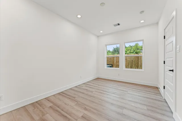 an empty room with wooden floor fan and windows