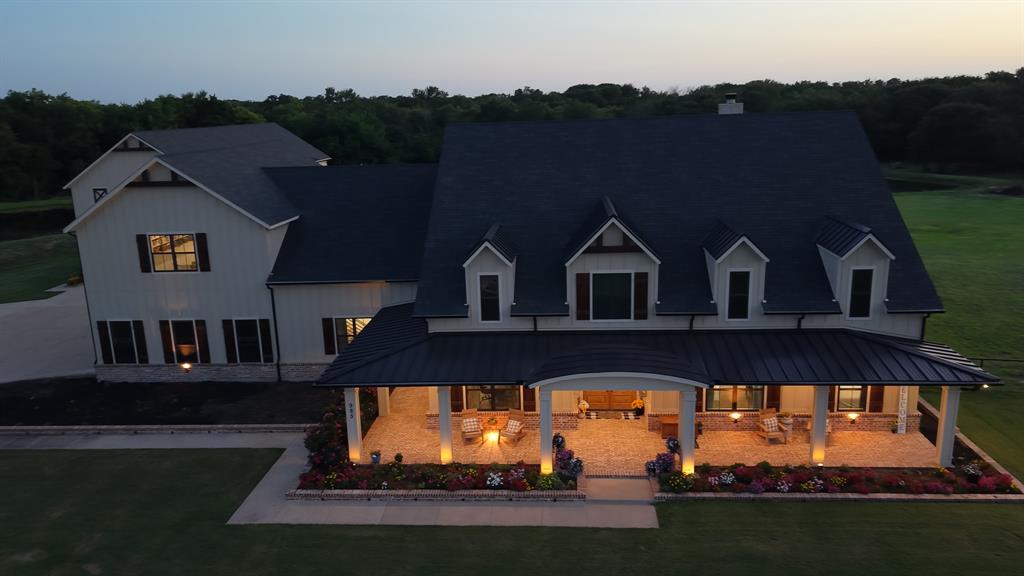 985 Vest Lane Pilot Point, TX 76258 - Photo 7 of 40 Spacious residence featuring board and batten siding, dark metal roofing, multiple dormer windows, a full-length covered porch with columns, and extensive landscaping