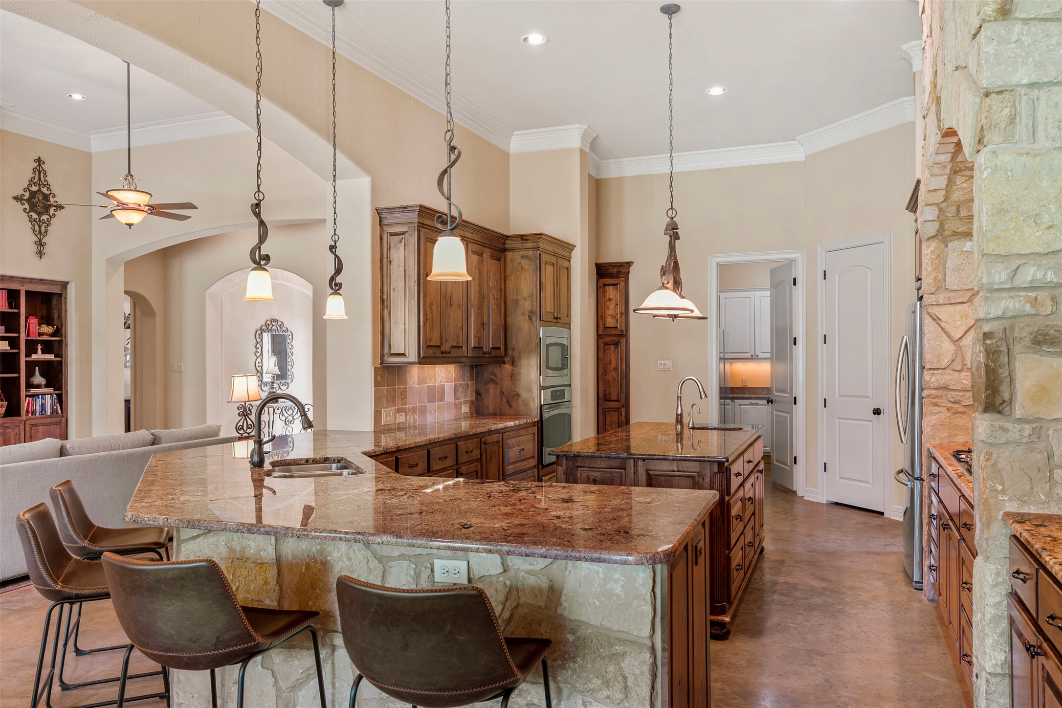 100 Portafino Lane Georgetown, TX 78633 - Photo 8 of 39 Kitchen featuring arched walkways, brown cabinets, a center island with sink, decorative backsplash, and ornamental molding