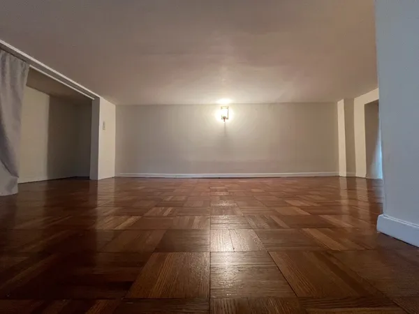 an empty room with wooden floor and windows with curtains