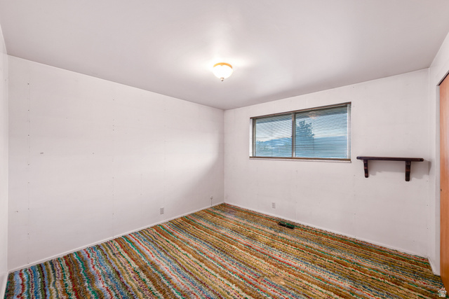 1940 West Old Hwy Road Morgan, UT 84050 - Photo 35 of 73 Room featuring a multi-colored striped carpet, a single window with horizontal blinds, a ceiling-mounted light fixture, and a wall-mounted wooden shelf