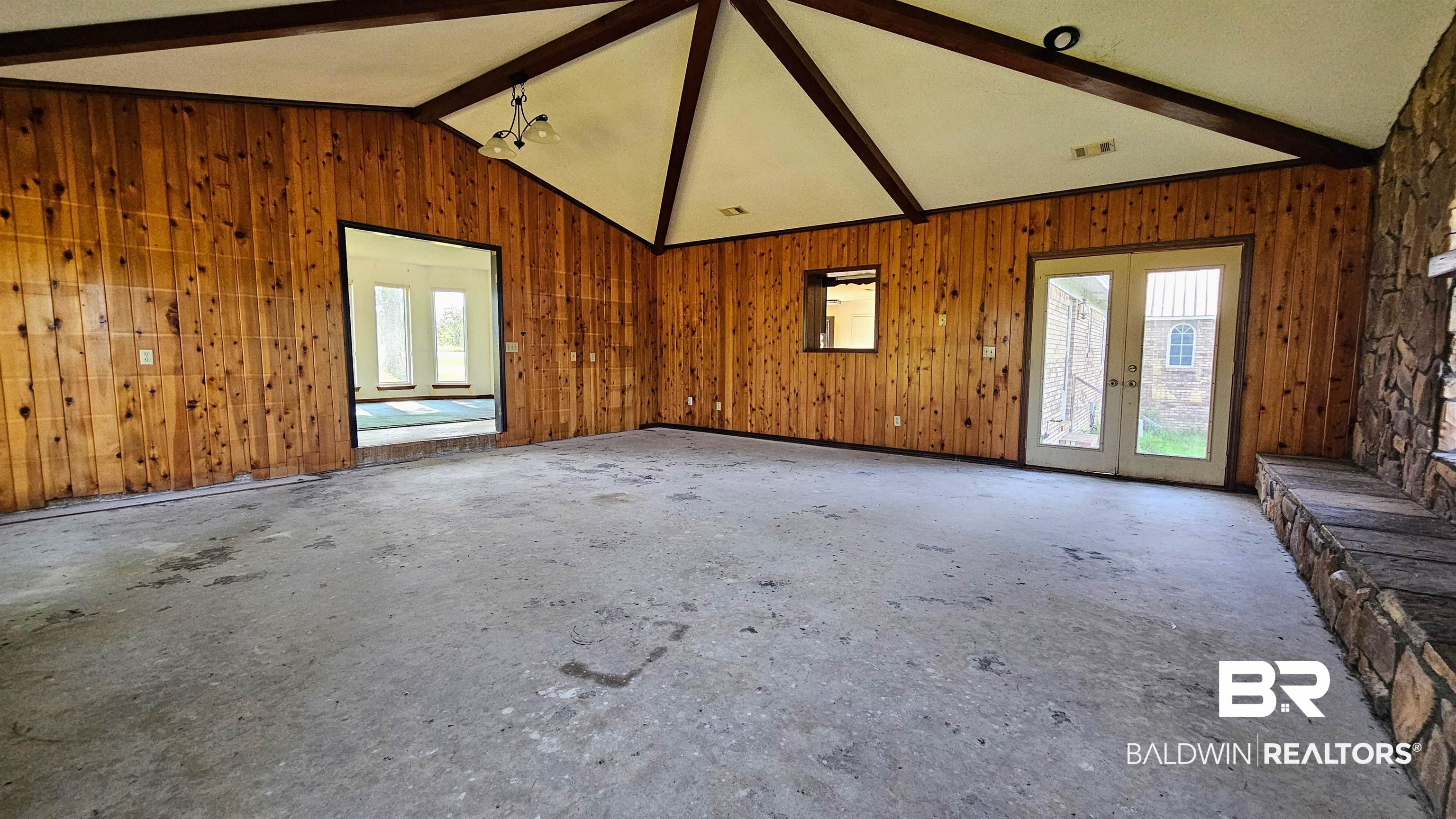 18824 Highway 41 Brewton, AL 36426 - Photo 19 of 40 Vaulted ceiling with exposed beams, wood-paneled walls, stone accent wall with integrated ledge, double glass French doors, and an open doorway to an additional room