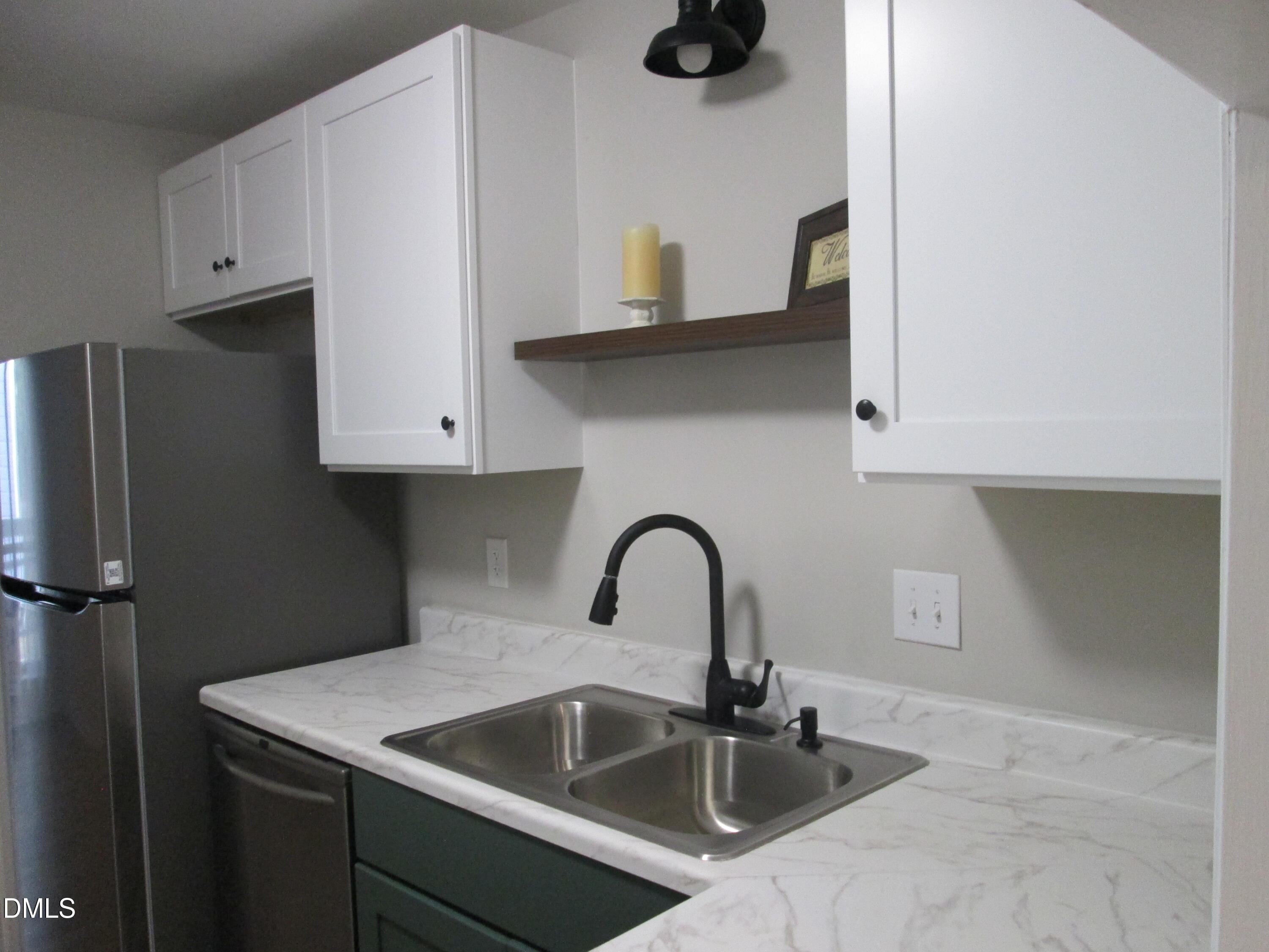 4651 Timbermill Court, Unit 103 Raleigh, NC 27612 - Photo 11 of 40 White shaker-style upper cabinetry, stainless steel double basin sink, matte black gooseneck faucet, light-toned countertops, and a built-in stainless steel dishwasher