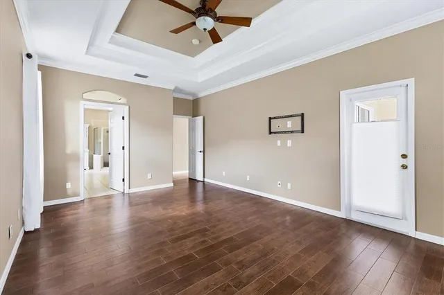 an empty room with a chandelier fan and wooden floor