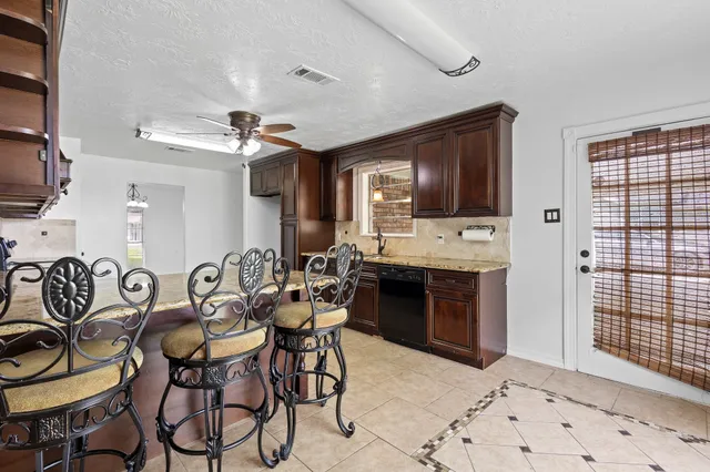 a kitchen with granite countertop stainless steel appliances lots of wooden cabinets a sink stove and chairs